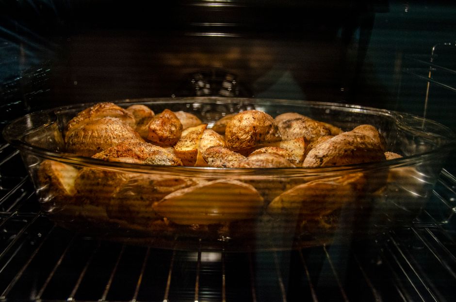 Through glass of appetizing unpeeled spicy potatoes in dish roasting in oven at home